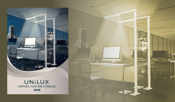 Un ufficio moderno con scrivanie, computer e lampade da terra alte. A sinistra, la copertina di un catalogo mostra UNILUX Lampade, Piantane e Orologi 2026, evidenziando le opzioni dei cataloghi. Lo spazio, illuminato in modo soffuso, crea un'atmosfera accogliente.